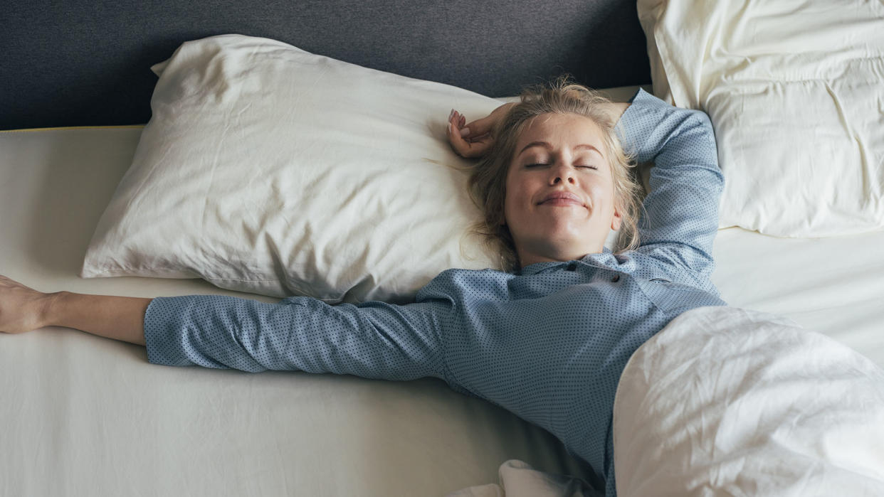  A woman wakes up and stretches in bed after enjoying a good night's sleep. 