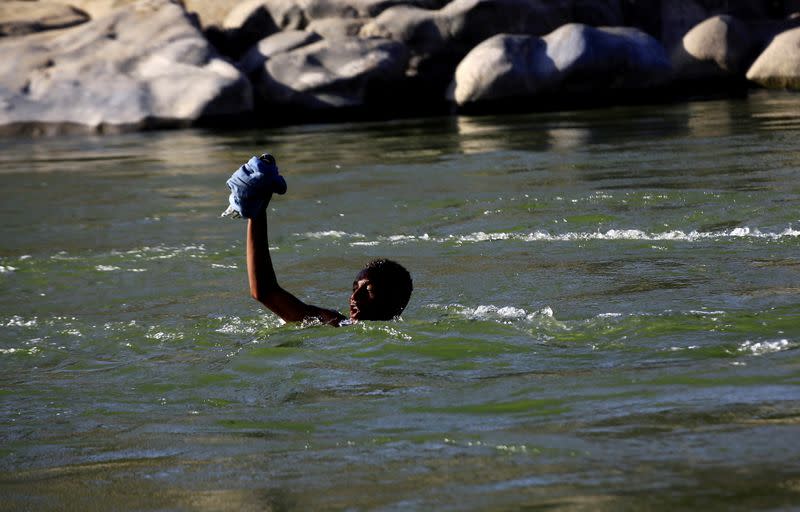An Ethiopian fleeing the ongoing fighting in Tigray region, lifts his clothes as he crosses the Setit river on the Sudan-Ethiopia border in Hamdayet village in eastern Kassala state