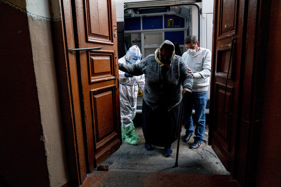 In this photo taken on Saturday, May 9, 2020, ambulance medic Svetlana Padynich, left, helps a patient suspected of having coronavirus to get into the regional hospital of Chernivtsi, Ukraine. Ambulance medics experience shortages of protective gear and many ambulance medics in the city got infected. (AP Photo/Evgeniy Maloletka)