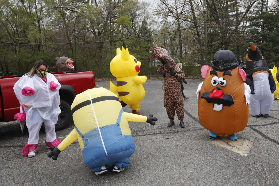 In this Monday, May 11, 2020 photo, members of the T-Rex Walking Club prepare for their walk through a neighborhood in Ferndale, Mich. While the club members get a kick out of their strolls through town, the idea is to bring a little bit of cheer to their fellow residents who remain under quarantine as part of Gov. Gretchen Whitmer’s stay-at-home order due to the COVID-19 pandemic. (AP Photo/Carlos Osorio)