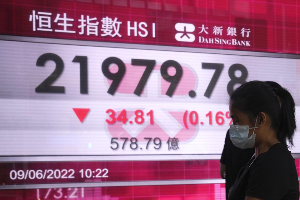 A woman wearing a face mask walks past a bank's electronic board showing the Hong Kong share index in Hong Kong, Thursday, June 9, 2022. Shares were mostly lower in Asia on Thursday as investors watched for fresh signs of inflation and crude oil prices hovered above $120 a barrel, adding to price pressures. (AP Photo/Kin Cheung)