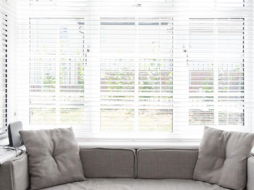 Window treatments with white trim and white blinds behind gray seat and pillows