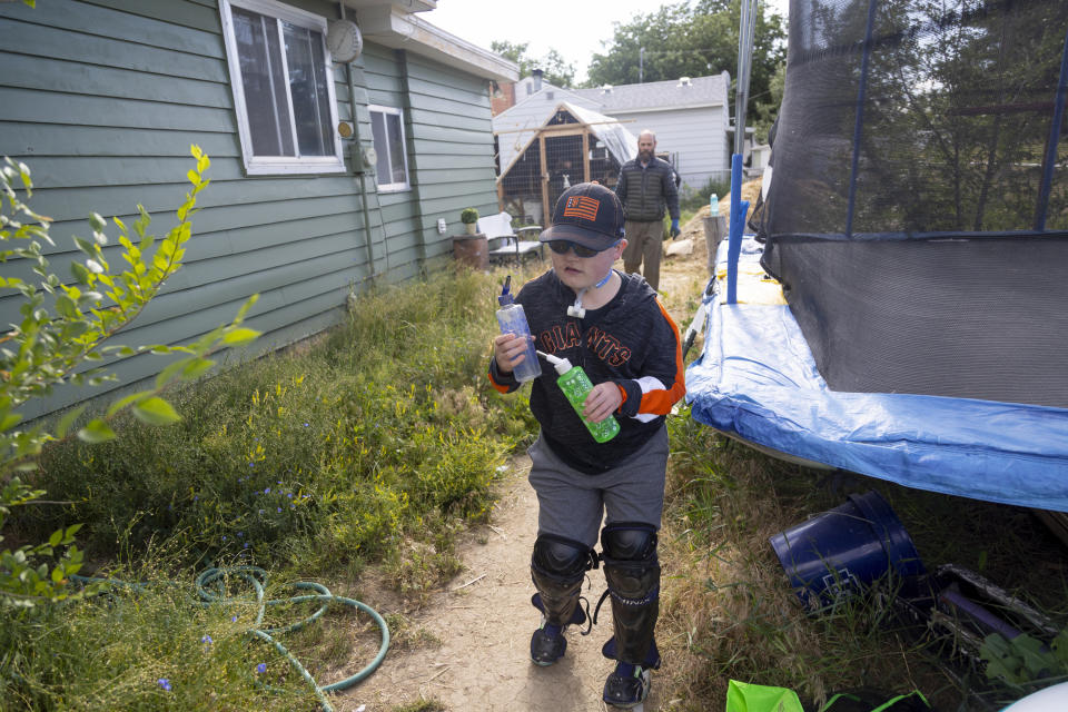 Brady Hill, 14, fills water bottles for home raised rabbits while being followed by his dad Nathan at their home in Meridian, Idaho, June 19, 2023. Brady survived a rare brain cancer as a baby, but requires round the clock care. Brady's brother Monte, 8, and sister Misha, 12, are also seen. Families of severely disabled children across the country are worried about the future of crucial Medicaid payments they started receiving to provide care during the COVID-19 pandemic. (AP Photo/Kyle Green)