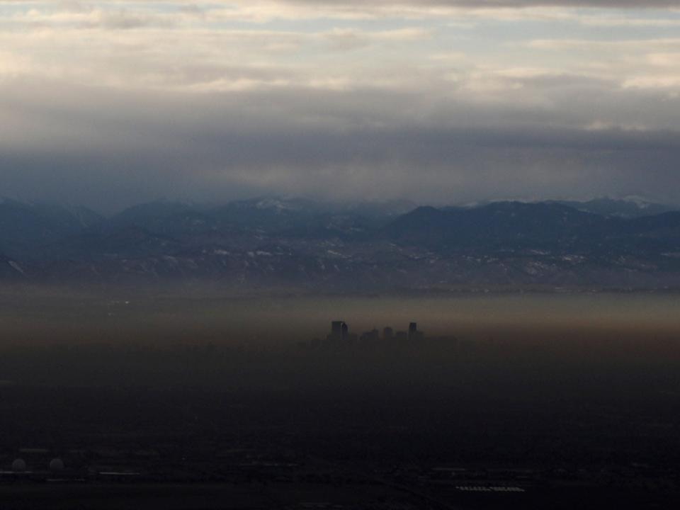 tall buildings poke out above layer of green brown smog in valley with mountains in the background