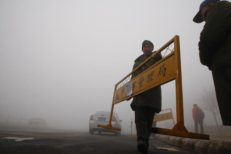 A workman carries a road barrier on a street under heavy smog in Harbin, northeast China's Heilongjiang province, on October 21, 2013