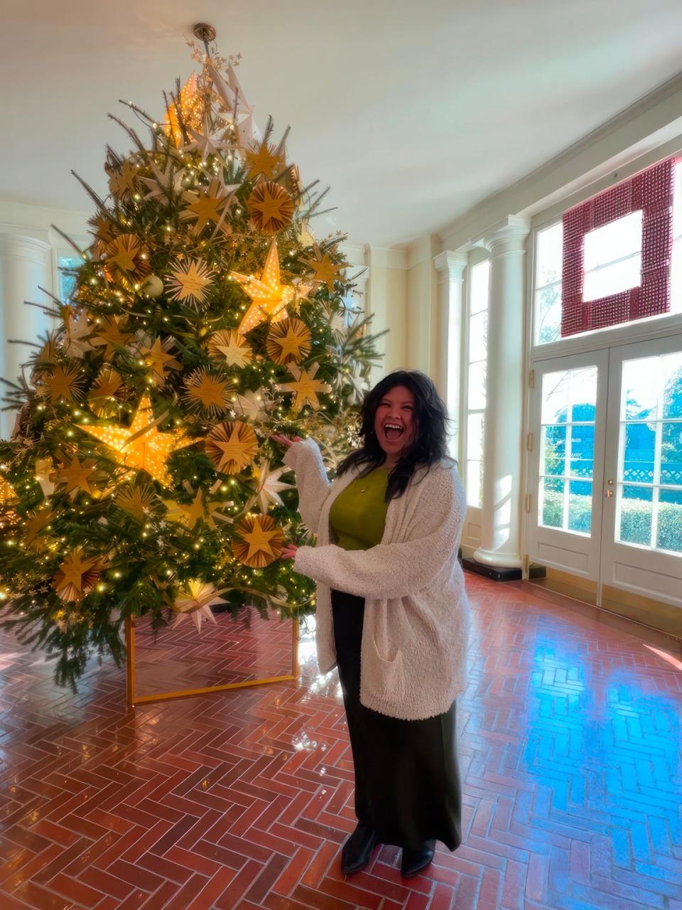 Kelly Marcelo stands in front of a White House Christmas tree she helped festoon with ornaments. Marcelo was among a dozen content creators selected from the social media platform, Pinterest, to help decorate the White House. About 300 volunteers also participated. The decorative theme unveiled Nov. 27, 2023 by Jill Biden was "Magic, Wonder, and Joy."