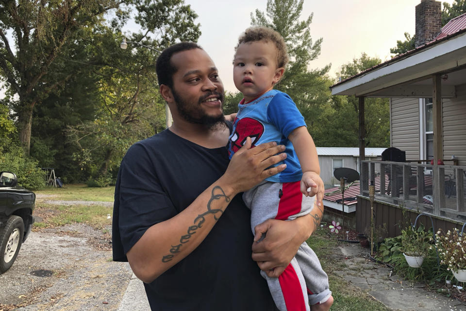 Nicholas Lewis holds son, Nick Jr., near their home in Vienna, Ill., on Sunday, Sept. 27, 2020. Nick Jr.'s grandmother, Maribeth Harris, says "It's our sanctuary," of the street where they live. One of her daughters lives next door. Another lives across the street with her boyfriend, Lewis. Three grandkids live with her while Lewis takes care of the fourth. Harris, her husband and their daughters are white. Lewis says, "I feel scared or just even strange going around to the store, because I know all eyes are on me." (AP Photo/Noreen Nasir)