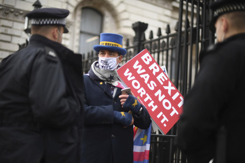 Police speak to anti-Brexit protestor Steve Bray, at the gates of Downing Street, London, Thursday, Dec. 24, 2020. Negotiators from the European Union and Britain worked through the night and into Christmas Eve to put the finishing touches on a trade deal that should avert a chaotic economic break between the two sides next week. Trade will change regardless come Jan. 1, when the U.K. leaves the bloc’s single market and customs union. (Victoria Jones/PA via AP)