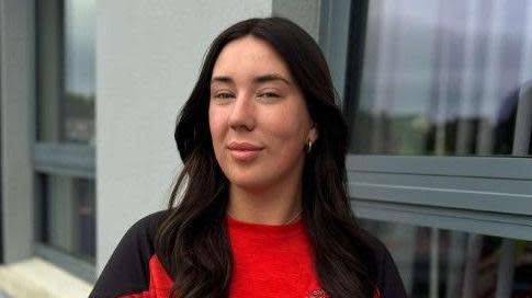 Shows Allie McGarrible with long black hair and in a red t-shirt