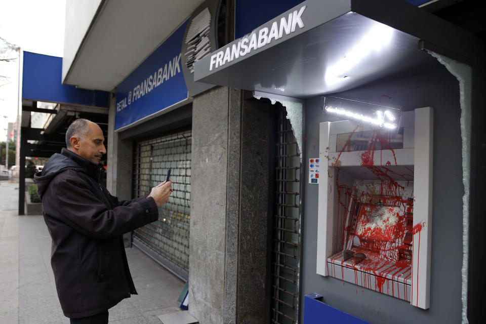 A man uses his phone to take a picture of ATM screen of Fransa Bank that was painted and damaged by anti-government protesters in Beirut, Lebanon, Wednesday, Jan. 15, 2020. Banks in Hamra trade street were badly damaged after a night that witnessed clashes between anti-government protesters and Lebanese riot police. (AP Photo/Bilal Hussein)