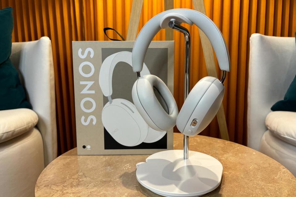 <p>White headphones on stand sitting on a small table with their box in the background.</p>
