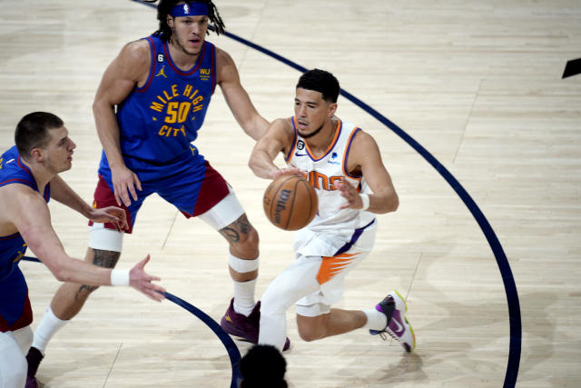 Phoenix Suns guard Devin Booker, right, passes the ball as Denver Nuggets center Nikola Jokic, left, and forward Aaron Gordon (50) defend in the first half of Game 1 of an NBA second-round basketball series Saturday, April 29, 2023, in Denver. (AP Photo/David Zalubowski)