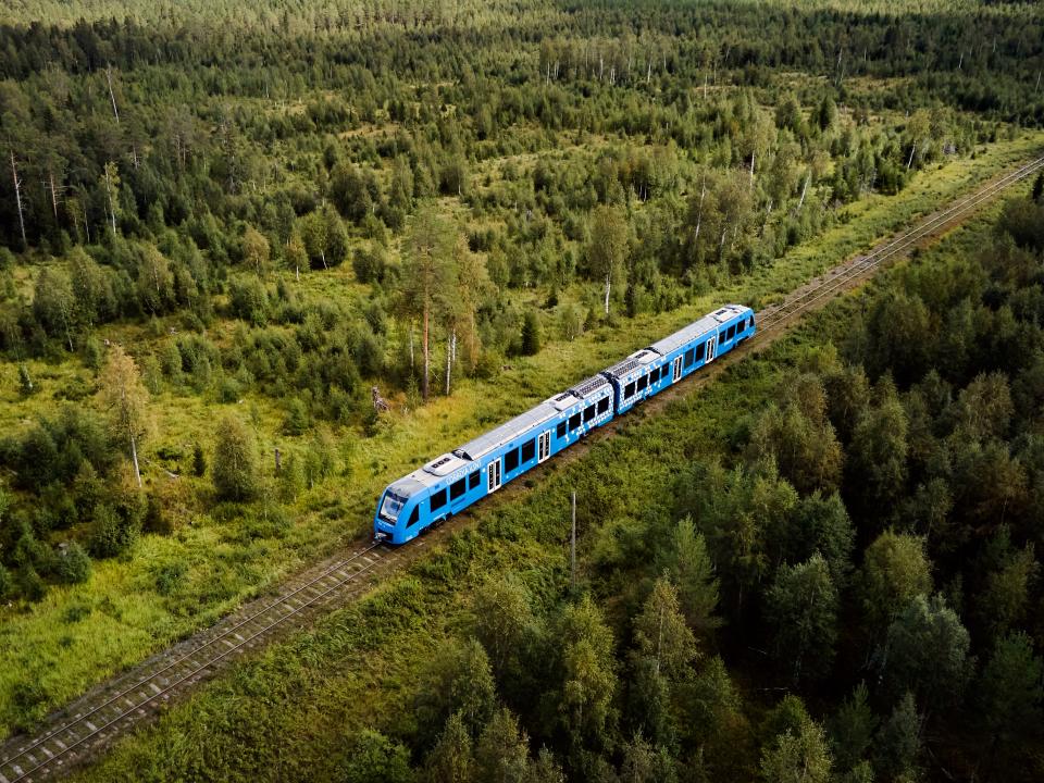 A blue Coradia iLint hydrogen-powered train running through the forest.