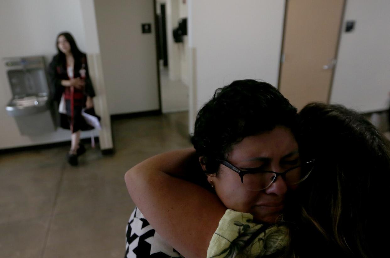 A woman is overcome with emotion and embraces another woman as a third woman stands beside a water fountain.