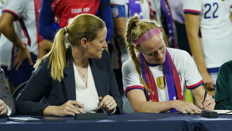 Cindy Parlow Cone, left, president of the U.S. Soccer Federation, looks on as United States’ Becky Sauerbrunn signs a new collective bargaining agreement at Audi Field, Tuesday, Sept. 6, 2022, in Washington. On Friday, Cone and U.S. Soccer announced a U.S.-Mexico joint bid to host the 2027 Women’s World Cup.