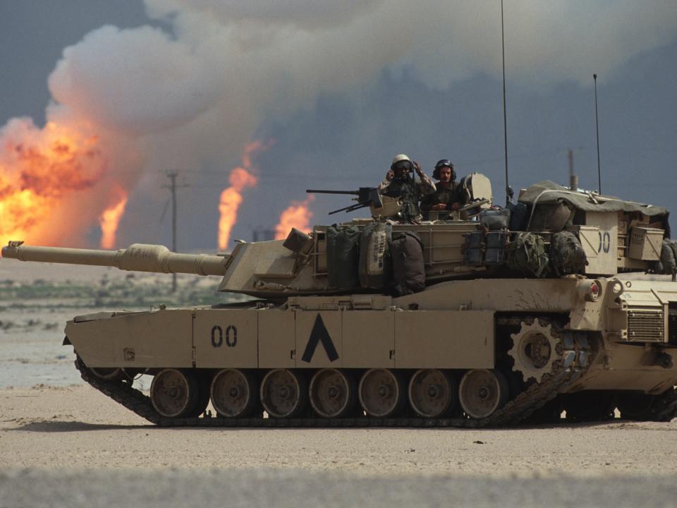 American soldiers operating an M1A1 Abrams tank as an oil wells burn in the distance,