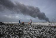 FILE- Sri Lankans salvage wreck washed off to the shore from the burning Singaporean ship MV X-Press Pearl which is anchored off Colombo port at Kapungoda, out skirts of Colombo, Sri Lanka, Wednesday, May 26, 2021. Fishing was banned in the area because of health risks associated with the chemicals in the water, affecting the livelihoods of some 4,300 families, who still have not received compensation. (AP Photo/Eranga Jayawardena, File)