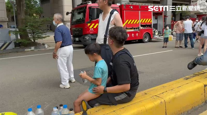 一名消防員於心不忍，把男童抱著坐腿上，另一名消防員則是叮嚀男童水要慢慢喝。(圖／記者羅欣怡拍攝)