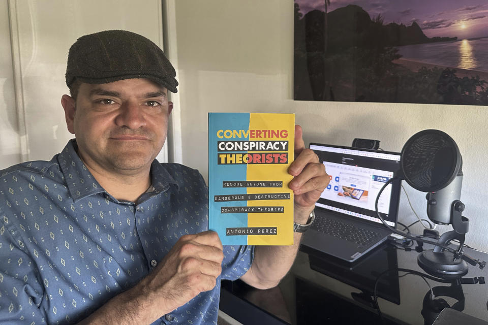 Antonio Perez holds his book "Converting Conspiracy Theorists" in Kauai, Hawaii on Nov. 5, 2023. “I was suicidal before I got into conspiracy theories,” said Perez, who became obsessed with Sept. 11 conspiracy theories and QAnon until he decided they were interfering with his life. Back then, when he first found other online conspiracy theorists, he was ecstatic. “It’s like: My God, I’ve finally found my people!” (AP Photo/Eugene Garcia)