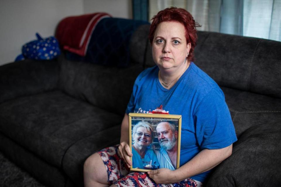 Kimberly Rhodus poses for a portrait holding a photograph of her father at her home in Richmond, Ky., Thursday, May 6, 2021. After her father died in 2016, his workers comp benefits were continuously deposited in their joint account for four years. Rhodus tried to figure out where the money was coming from, but was unable to come to a conclusion. Last year an official announced to Rhodus that she owed the state $56,000.