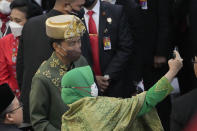 A member of the parliament takes a selfie with Indonesian President Joko Widodo who is wearing the traditional Bangka Belitung outfit, after he delivered his annual State of the Nation Address ahead of the country's Independence Day, at the parliament building in Jakarta, Indonesia, Tuesday, Aug. 16, 2022. (AP Photo/Tatan Syuflana, Pool)