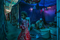 A young Rohingya refugee girl walks past an elderly man sitting inside a tent at a refugee camp alongside the banks of the Yamuna River in the south-eastern borders of New Delhi, sprawling Indian capital, July 1, 2021. Millions of refugees living in crowded camps are waiting for their COVID-19 vaccines. For months, the World Health Organization urged countries to prioritize immunizing refugees, placing them in the second priority group for at-risk people, alongside those with serious health conditions. (AP Photo/Altaf Qadri)