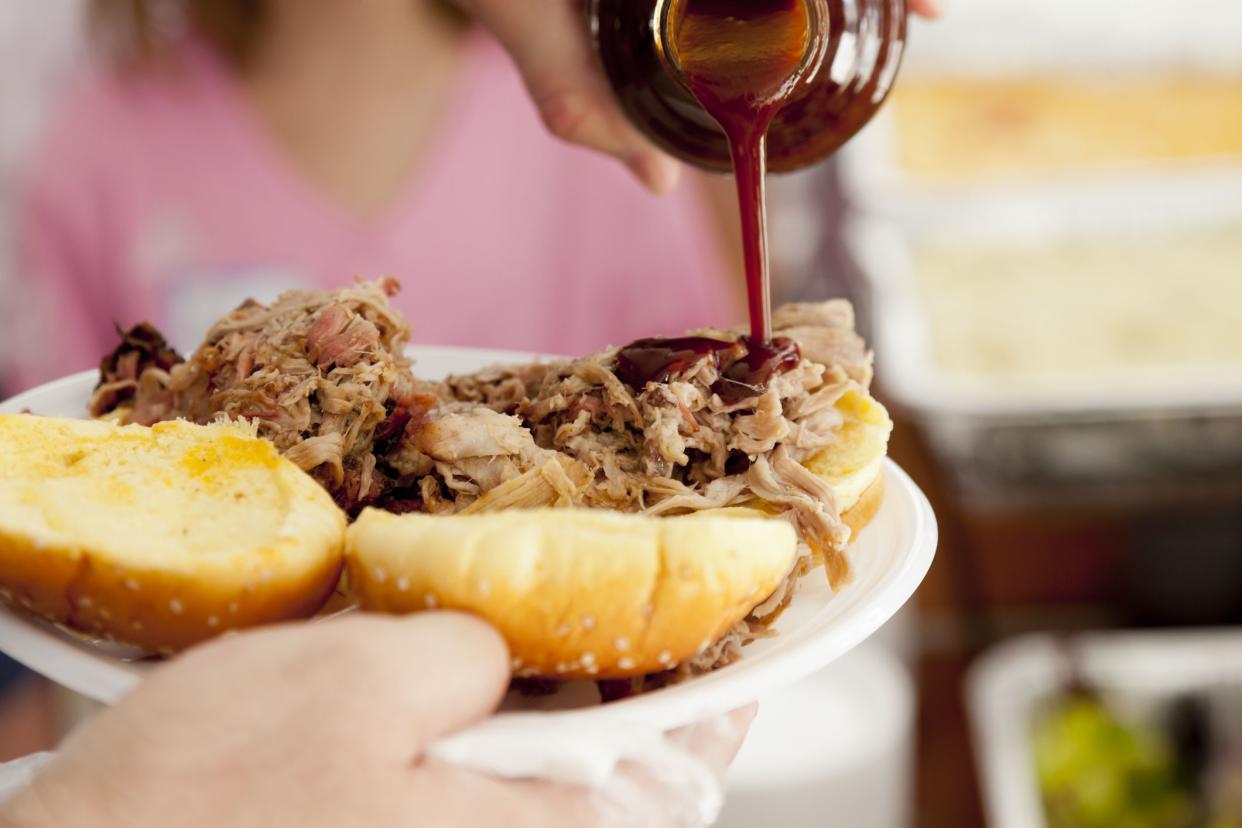 Adding barbeque sauce to a pulled pork sandwich.