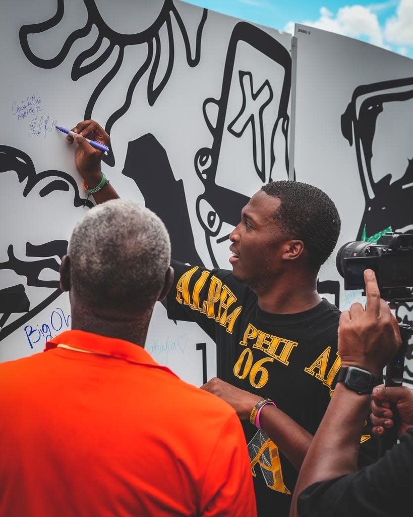 Florida A&M University graduate and artist Elijah Rutland signs his mural on FAMU's campus on Friday, Aug. 26, 2022 in partnership with Xfinity's HBCU Tour. His father Charles Rutland, also a FAMU alumnus, watches as he signs his name.