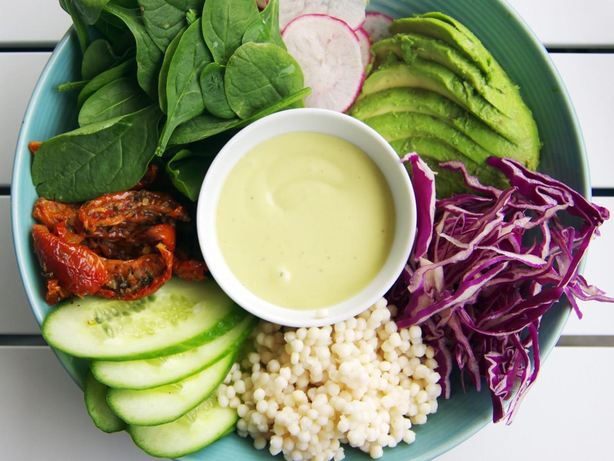 Vegan breakfast of pearl couscous and raw vegetables: cucumber, sundried-tomatoes, baby spinach, radish, avocado, and red cabbage with aioli