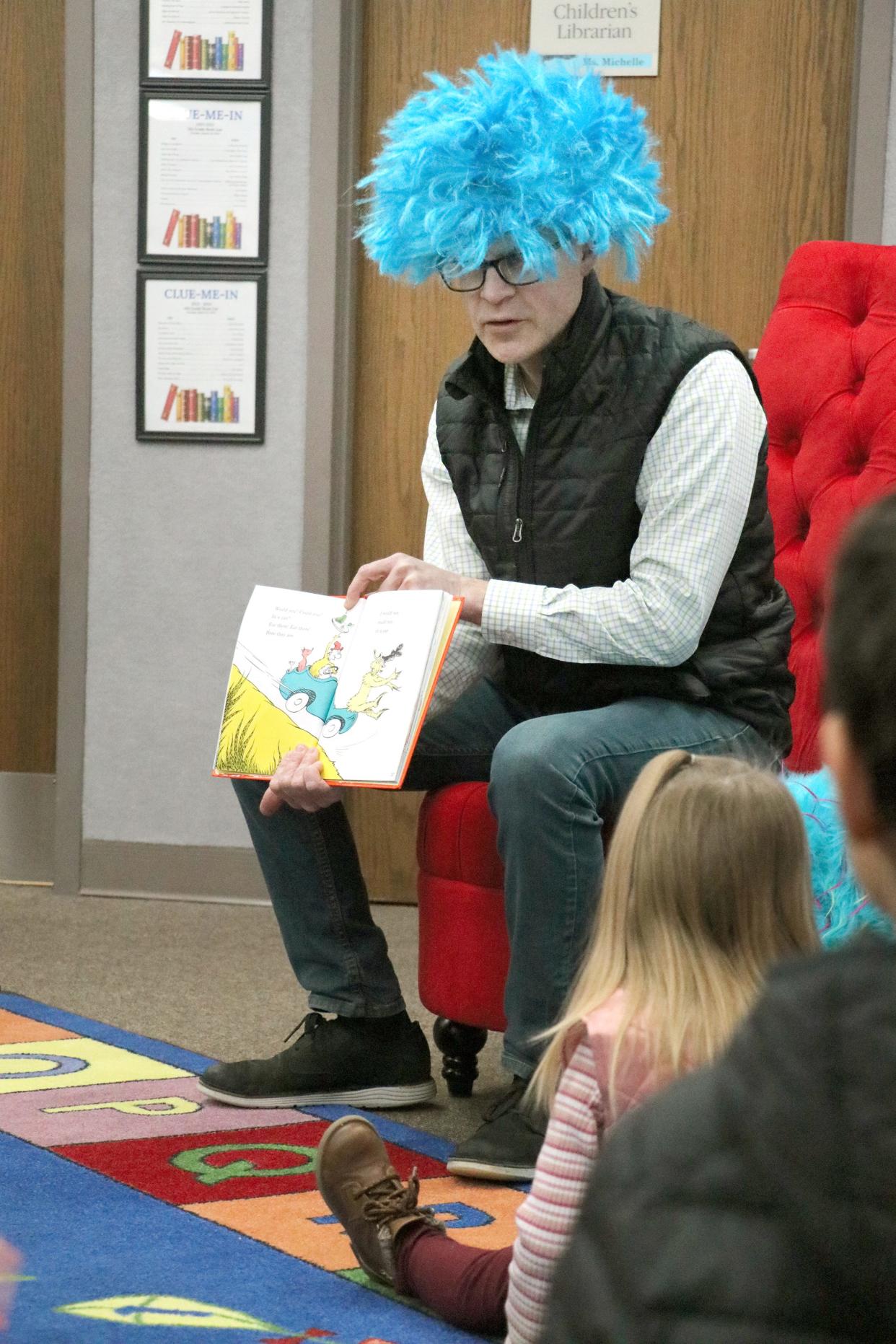 Sturgis Public Schools Superintendent Art Ebert, wearing a blue “Thing” wig, reads a Dr. Seuss book to a group of children gathered at Sturgis District Library.