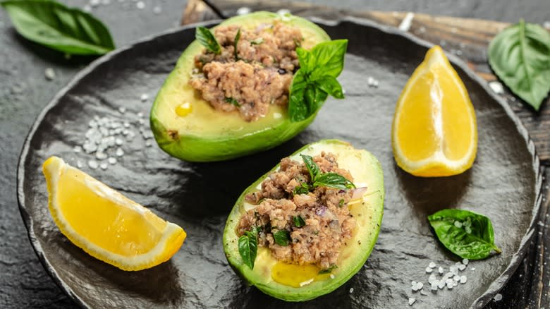 tuna salad inside avocado halves on a dark plate