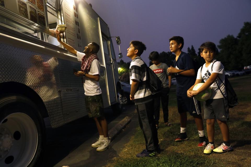 Young Afghan boys wait at a food cart at a park