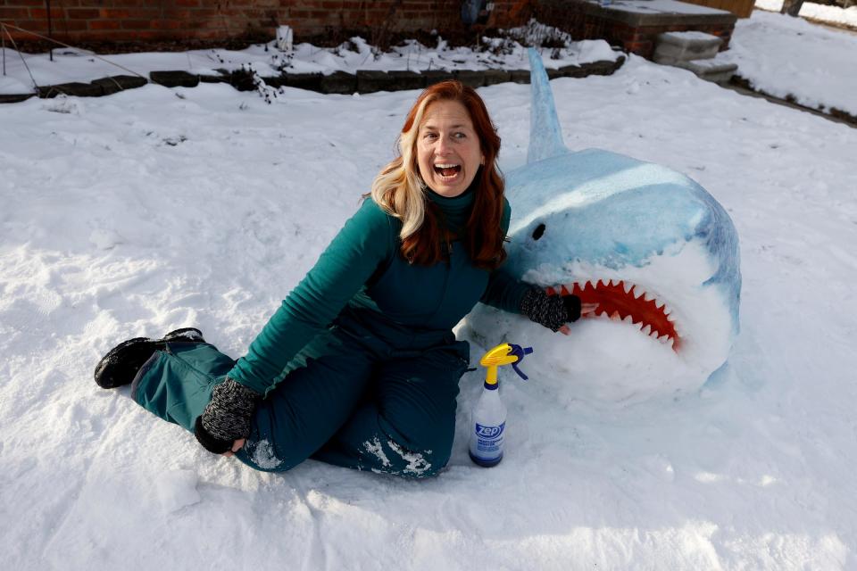 Jennifer Ramirez, of Madison Heights, has fun Tuesday, Jan. 31, 2023, with one of the great white sharks she sculpted out of snow on her front lawn. Ramirez, an art teacher, said it took her four to five hours to make the sculptures last weekend.