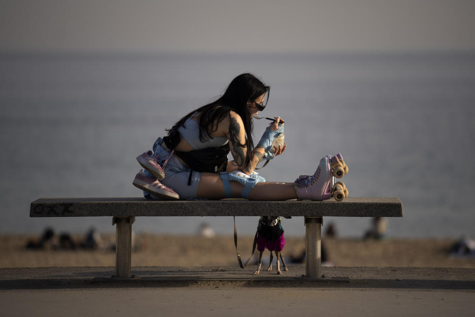 A woman eats an ice cream as people sunbathe on the beach in Barcelona, Spain, Friday, Jan. 26, 2024. Spain's weather agency says recent abnormally high temperatures for this time of year are set to continue in many parts of Spain on Friday and over the weekend, with an almost summer-like feeling in many coastal areas as people take to the beaches to sunbathe and some to have a winter swim(AP Photo/Emilio Morenatti)