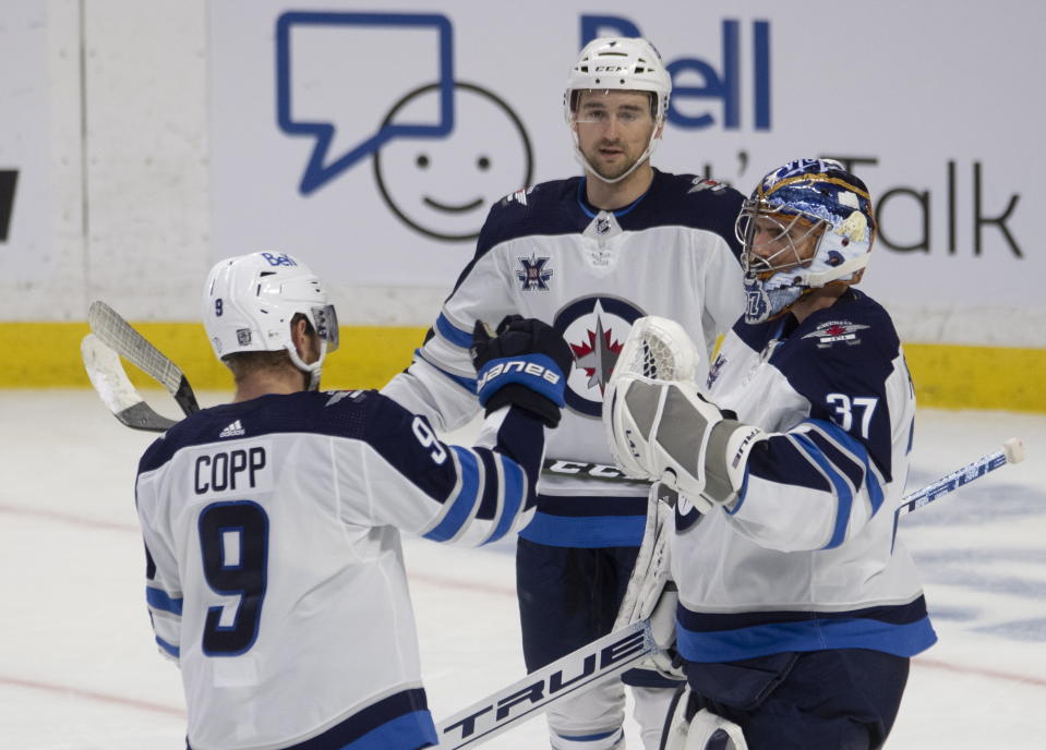 Winnipeg Jets' Neal Pionk, rear, Andrew Copp, and goaltender Connor Hellebuyck celebrate the team's win over the Ottawa Senators in an NHL hockey game Thursday, Jan. 21, 2021, in Ottawa, Ontario. (Adrian Wyld/The Canadian Press via AP)