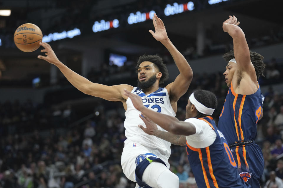 Minnesota Timberwolves center Karl-Anthony Towns, left, passes the ball while defended by New York Knicks forward Cam Reddish (0) and center Jericho Sims, right, during the first half of an NBA basketball game, Monday, Nov. 7, 2022, in Minneapolis. (AP Photo/Abbie Parr)