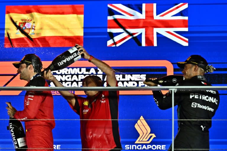 Le patron de l'écurie Ferrari Frederic Vasseur (au centre) et le pilote Mercedes Lewis Hamilton(à droite) arrosent de vin mousseux Carlos Sainz (à gauche), vainqueur du Grand Prix de Singapour 2023, sur le circuit de Marina Bay le 17 septembre 2023. (Lillian SUWANRUMPHA)
