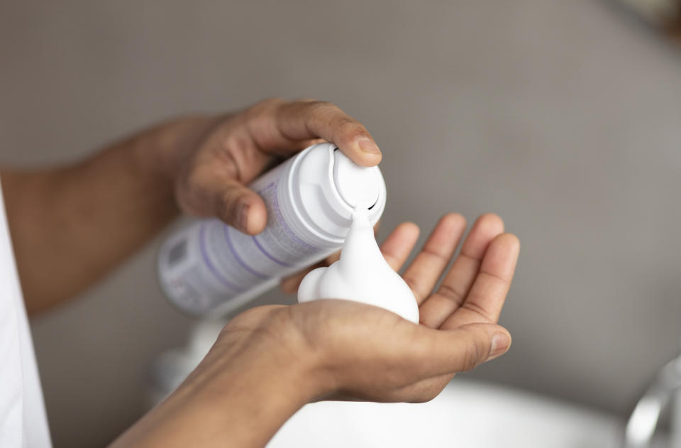 A close-up of a person dispensing white foam from a can onto their hand