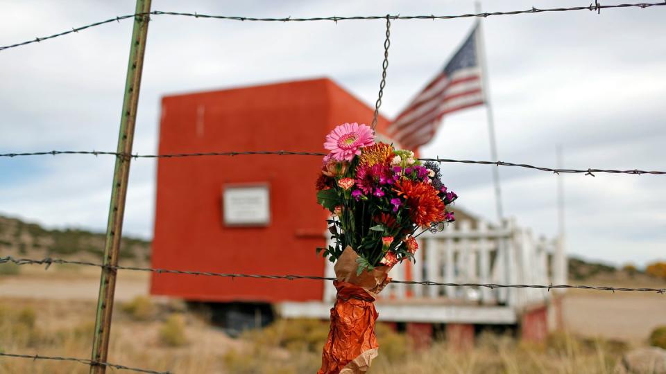 Blumenkranz hängt an einem Stacheldrahtzaun vor einem roten Container mit Veranda und US-Flagge