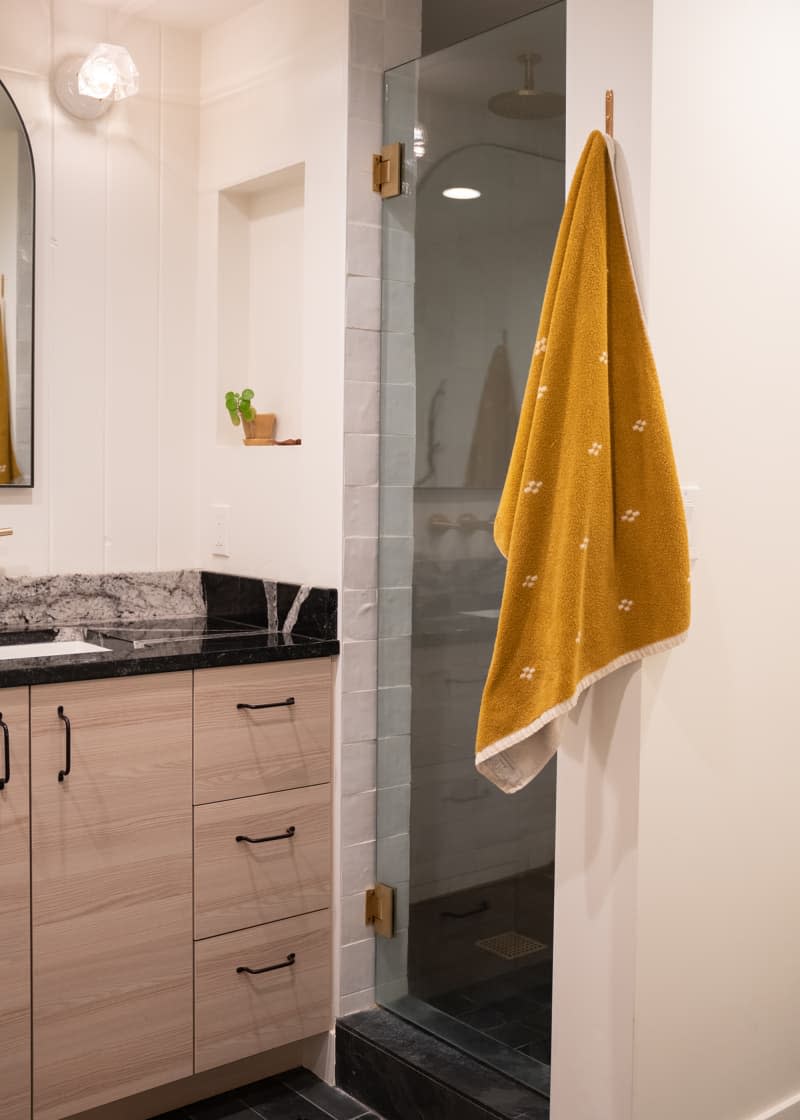 Towel hanging on bathroom hook beside glass shower.