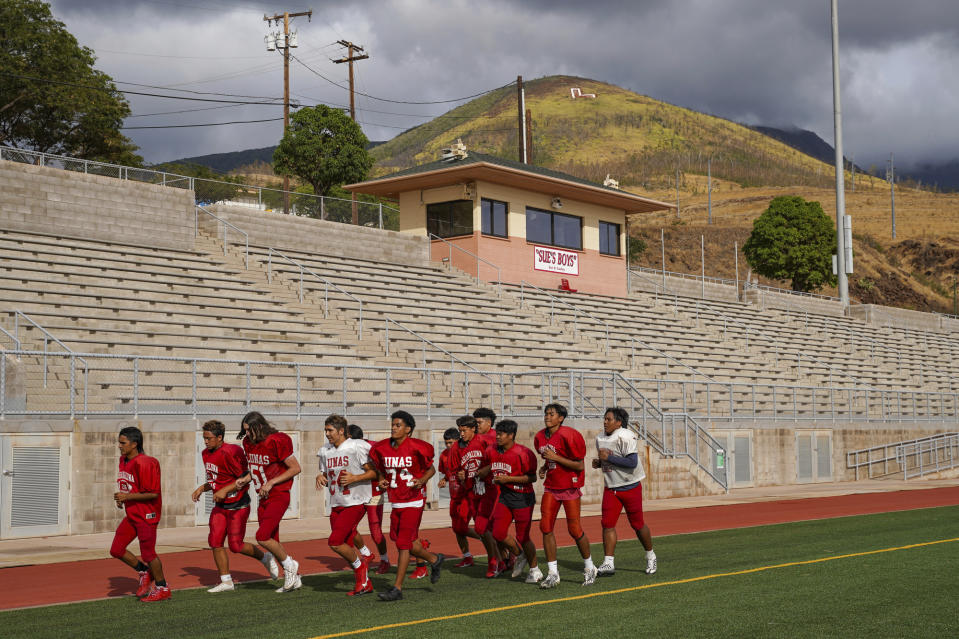 Lahainaluna High School football team players run around the field at Sue D. Cooley Stadium during their first week returning to practice on campus after August's wildfire Tuesday, Oct. 10, 2023, in Lahaina, Hawaii. Lahainaluna’s varsity and junior varsity football teams are getting back to normal since the devastating wildfire in August. (AP Photo/Mengshin Lin)