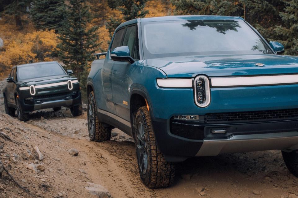 Two all electric Rivian R1Ts climbing a muddy hill. 