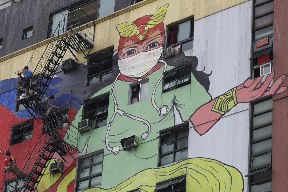 Artists paint an image of Darna, a fictional Filipino comics superhero, wearing a protective mask and scrub suit to honor health workers and frontliners in their fight against the new coronavirus on a building in Manila, Philippines on Monday, May 18, 2020. Crowds and vehicular traffic returned to shopping malls in the Philippine capital after a two-month coronavirus lockdown was partially relaxed over the weekend, prompting police to warn of arrests and store closures. (AP Photo/Aaron Favila)