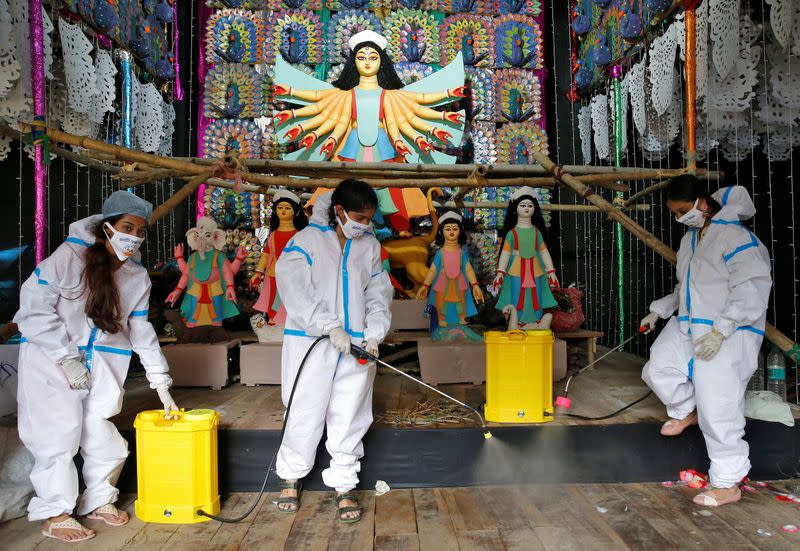 Women wearing personal protective equipment sanitize a "pandal" ahead of Durga Puja festival in Kolkata
