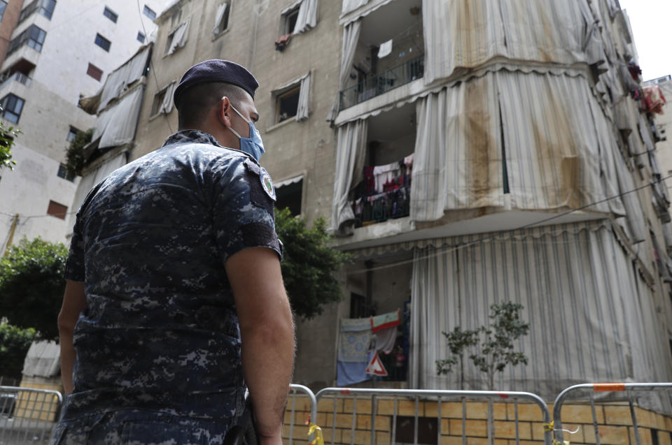 In this Saturday, May 23, 2020 photo, a Lebanese policeman is deployed to enforce isolation outside a building where dozens of foreign workers living in overcrowded apartments have tested positive with the coronavirus, in Beirut, Lebanon. Some 250,000 registered migrant laborers in Lebanon — maids, garbage collectors, farm hands and construction workers — are growing more desperate as a crippling economic and financial crisis sets in, coupled with coronavirus restrictions. With no functioning airports and exorbitant costs of repatriation flights, many are trapped, unable to go home. (AP Photo/Hussein Malla)