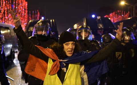 A protester wearing a "Yellow vest" (gilet jaune) demonstrates in front of a row of French police on the Champs-Elysees in Paris  - Credit: AFP