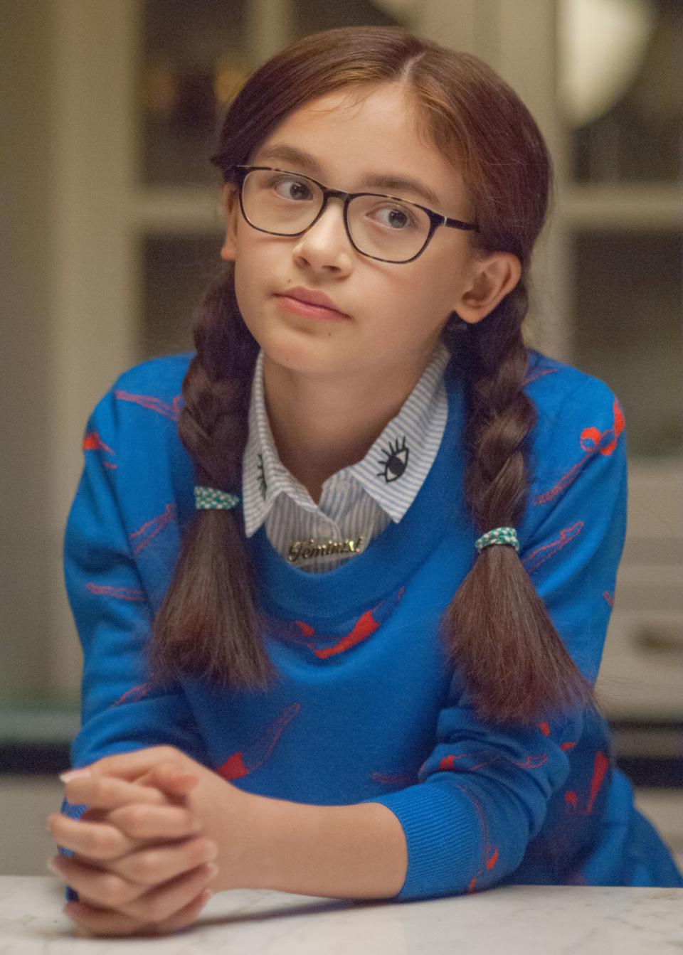 Anna Cathcart with braided hair wearing glasses and a patterned sweater