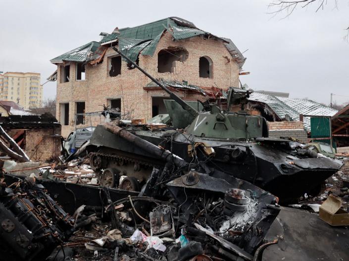 destroyed armored vehicle sits amid rubble in front of damaged house in bucha ukraine