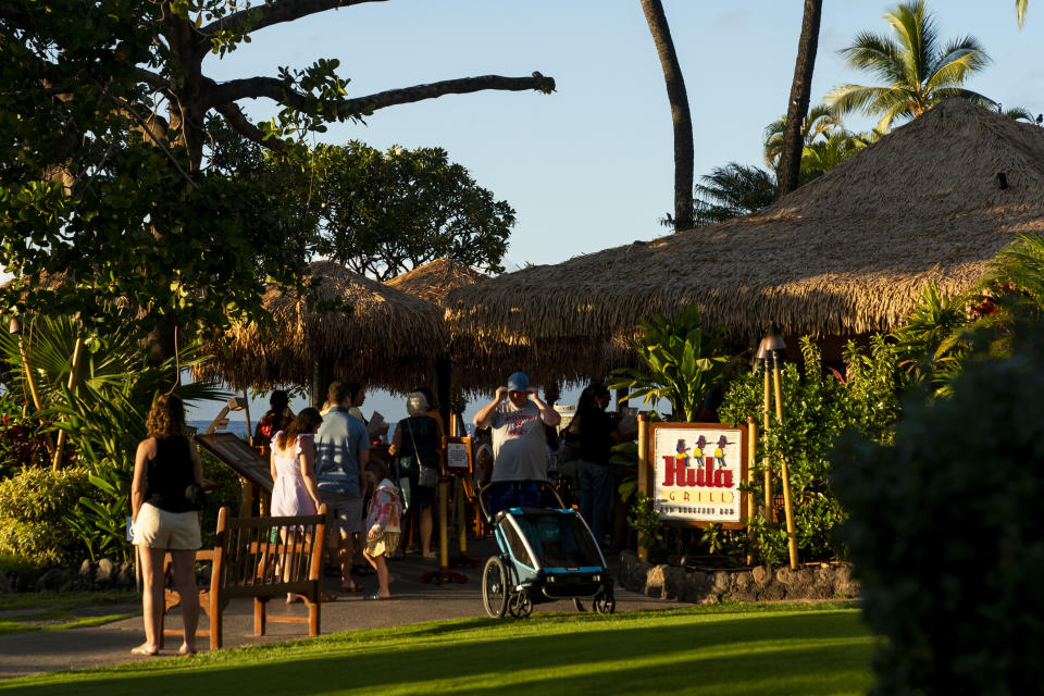 Tourists visit the Hula Grill on Kaanapali Beach, Wednesday, Dec. 6, 2023, in Lahaina, Hawaii. Residents and survivors still dealing with the aftermath of the August wildfires in Lahaina have mixed feelings as tourists begin to return to the west side of Maui. (AP Photo/Lindsey Wasson)