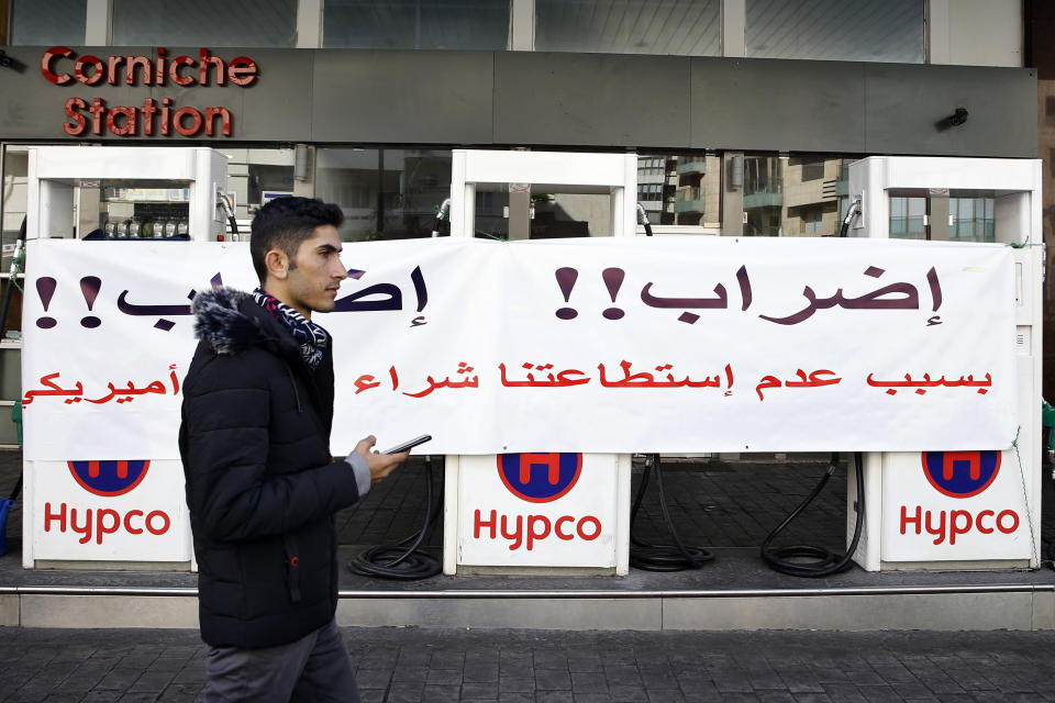 A man passes by a gas station that is closed during a protest against tight supply of dollars from the central bank in Beirut, Lebanon, Friday, Nov. 29, 2019. The Arabic banner reads: "Strike!! Strike!! Because we cannot purchase the U.S. dollar." The Lebanon's economic emergency has ignited nationwide protests against allegations of widespread corruption and mismanagement, bringing the country to a standstill. (AP Photo/Bilal Hussein)